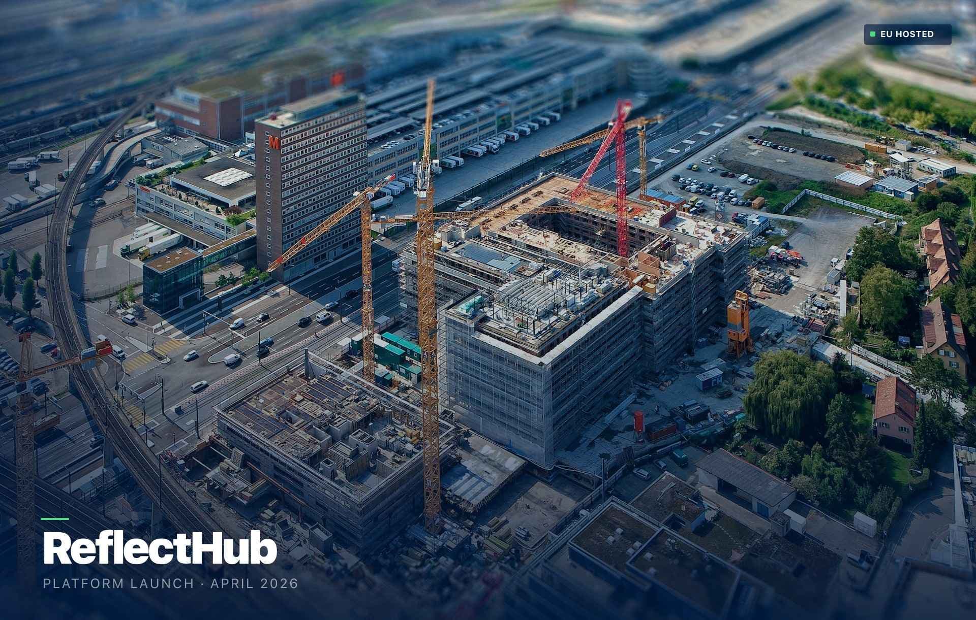 Aerial drone view of an urban construction site with tower cranes rising over a concrete building frame beside railway lines