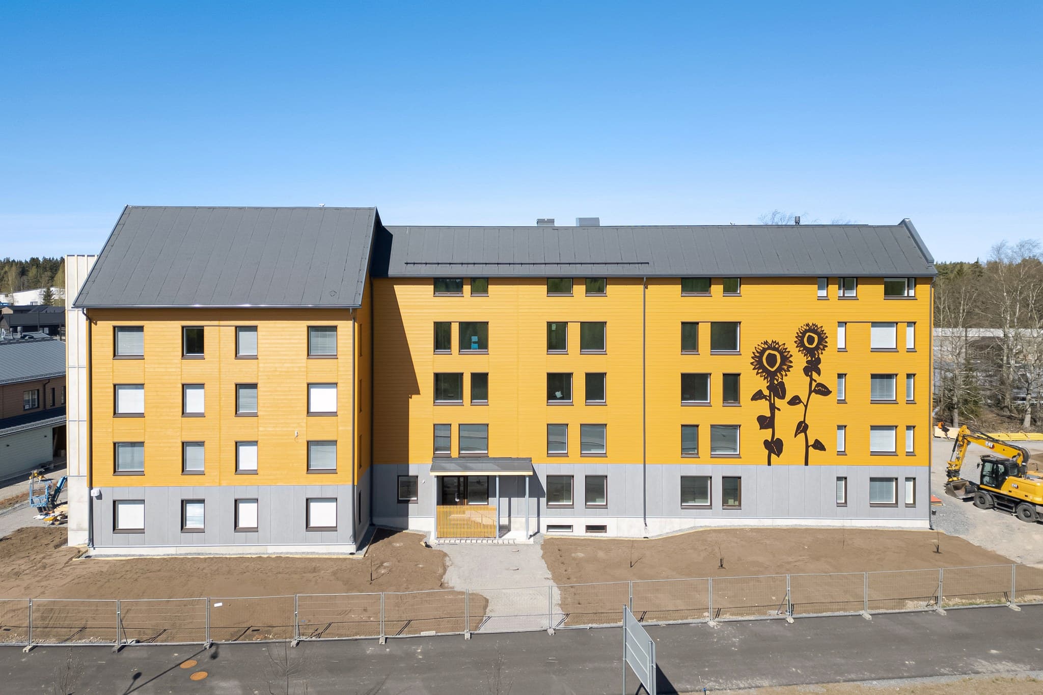 Neljakorruseline kortermaja ookerkollase puitfassaadi, halli sokli ja suure päevalillemaalinguga